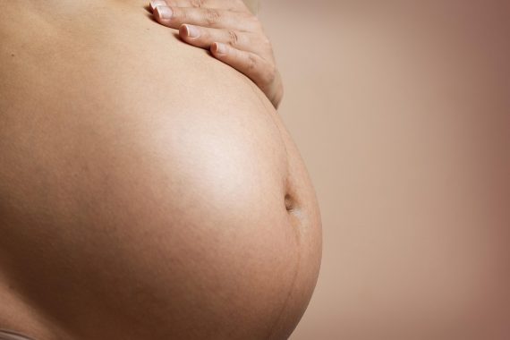 Kobieta w ciąży trzymająca się za brzuch dłonią, widoczny duży brzuch ciążowy.